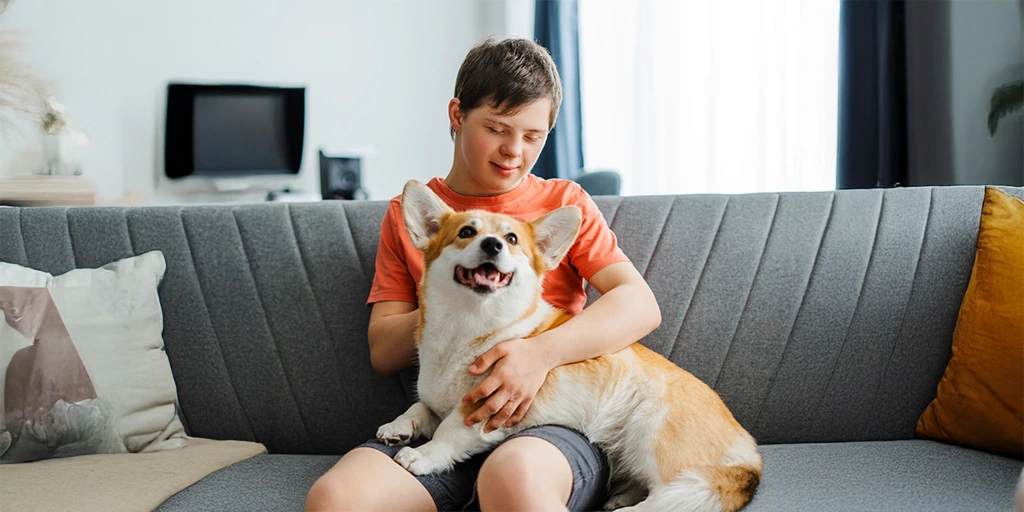 Smiling boy sitting on a couch, holding his happy corgi — showcasing the joy of a safe and loving bond.