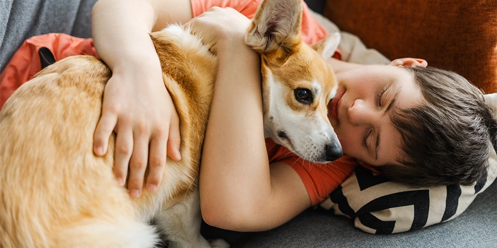 Boy cuddling with his dog on the couch, both appearing calm and secure — a comforting moment of companionship.