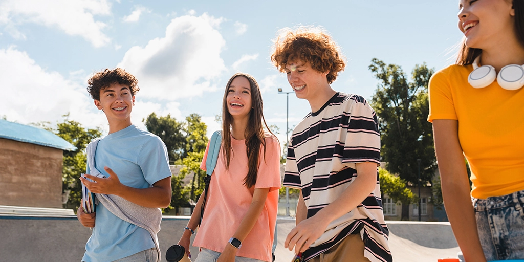 A group of teenagers walking and laughing together in a sunny park, illustrating the importance of fostering authentic social connections in autism.
