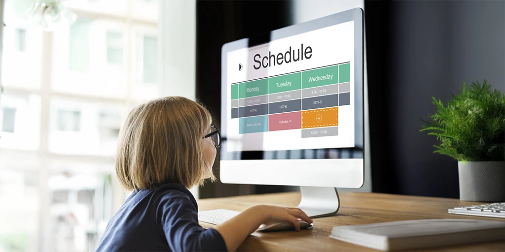 Young girl with glasses looking at a daily schedule displayed on a computer screen, suggesting structured routines.
